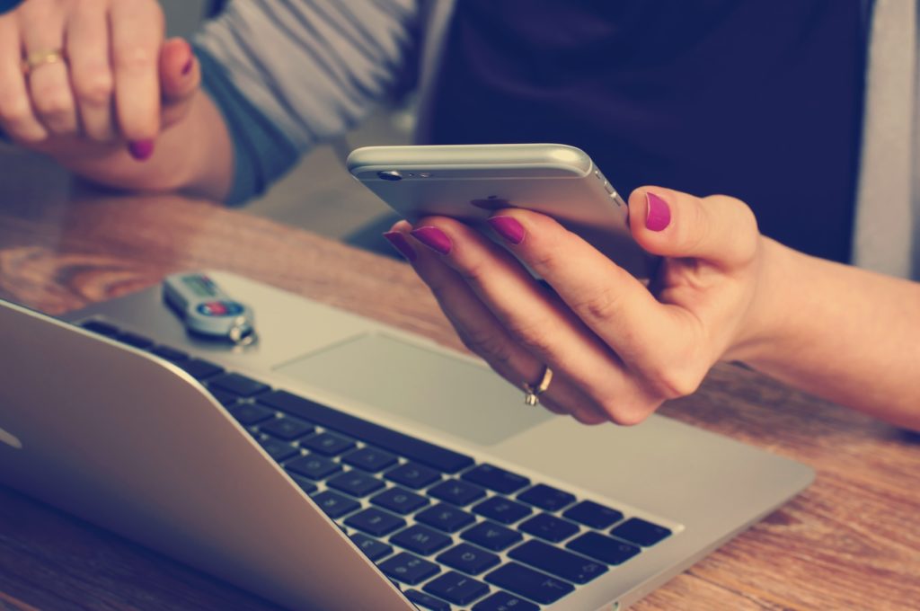 Woman holding her smartphone at her laptop, presumably looking for services online